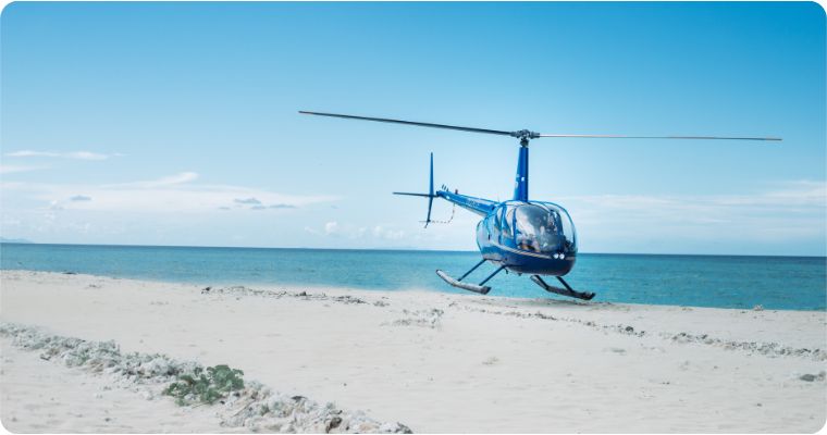 Blue helicopter taking off from white sand beach 